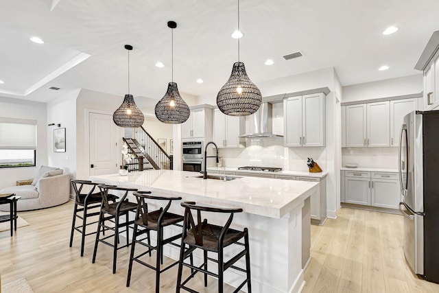 kitchen featuring sink, wall chimney exhaust hood, hanging light fixtures, light hardwood / wood-style flooring, and appliances with stainless steel finishes