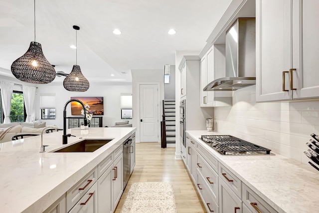 kitchen with light stone countertops, sink, wall chimney range hood, decorative light fixtures, and light wood-type flooring