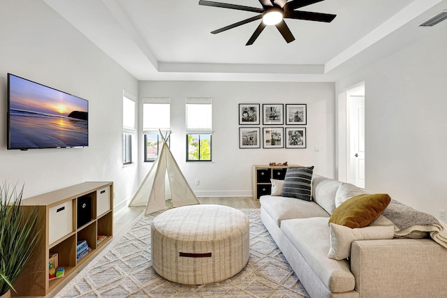 living room with a tray ceiling, ceiling fan, and light hardwood / wood-style floors