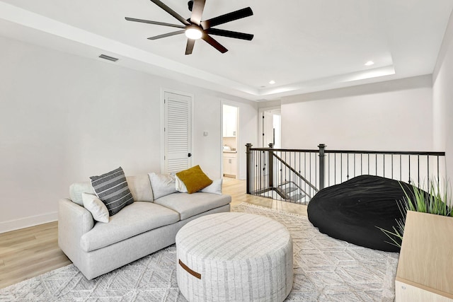 living room with ceiling fan, a raised ceiling, and light hardwood / wood-style flooring