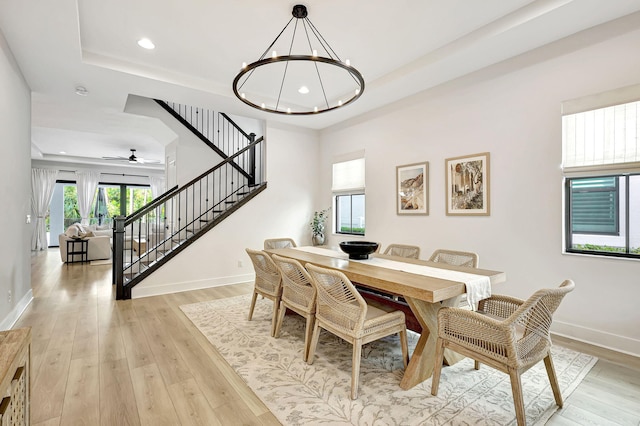 dining room with ceiling fan with notable chandelier, light wood-type flooring, and a tray ceiling