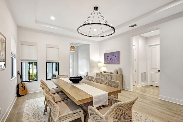 dining area with light hardwood / wood-style floors, a raised ceiling, and a notable chandelier