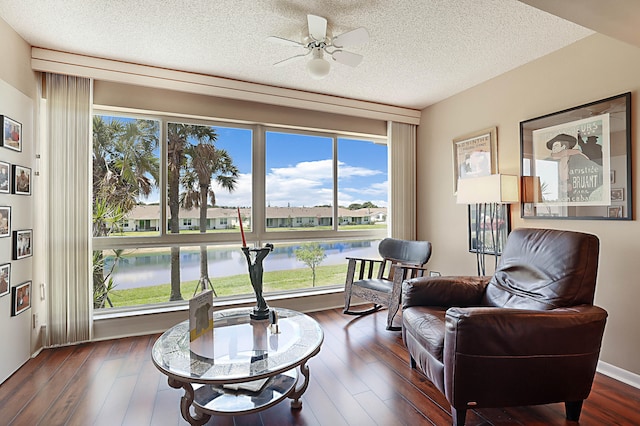 living area with dark hardwood / wood-style floors, a textured ceiling, a water view, and ceiling fan