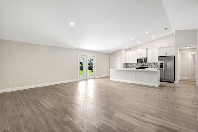 unfurnished living room with french doors, lofted ceiling, and light hardwood / wood-style flooring