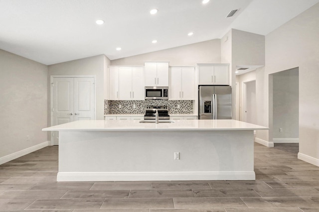 kitchen featuring white cabinetry, vaulted ceiling, stainless steel appliances, a kitchen island with sink, and backsplash