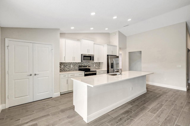 kitchen featuring lofted ceiling, appliances with stainless steel finishes, an island with sink, and white cabinets