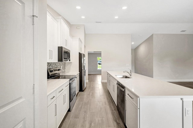 kitchen with sink, appliances with stainless steel finishes, white cabinetry, backsplash, and a kitchen island with sink