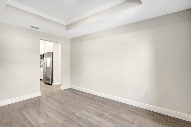 spare room featuring crown molding, light hardwood / wood-style flooring, and a raised ceiling