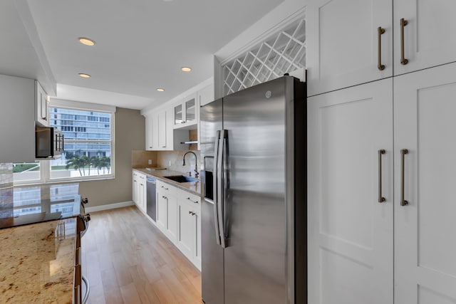 kitchen featuring white cabinets, appliances with stainless steel finishes, light stone countertops, light hardwood / wood-style floors, and sink