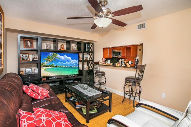 living room featuring light hardwood / wood-style floors, a textured ceiling, and ceiling fan