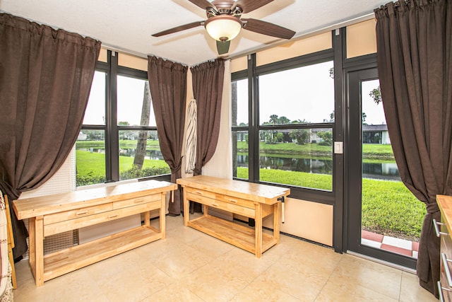 sunroom with plenty of natural light, a water view, and ceiling fan