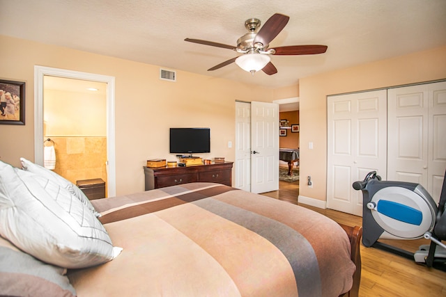 bedroom with light hardwood / wood-style floors, multiple closets, ensuite bath, and ceiling fan