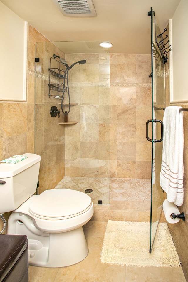 bathroom featuring a shower with door, toilet, tile patterned floors, and tile walls