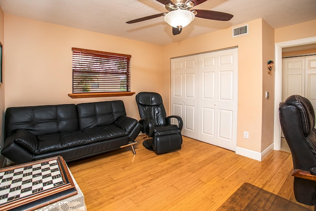 living room featuring a textured ceiling, light wood-type flooring, and ceiling fan