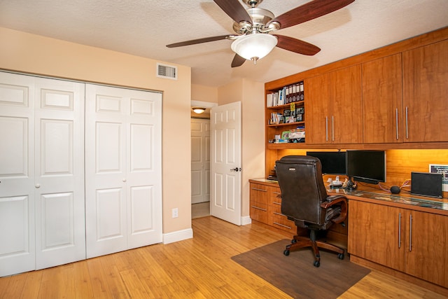 home office with built in desk, ceiling fan, a textured ceiling, and light hardwood / wood-style flooring