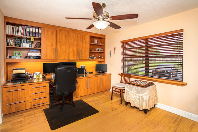 home office featuring built in desk, a textured ceiling, light wood-type flooring, and ceiling fan