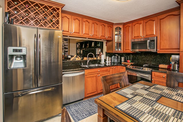 kitchen featuring tasteful backsplash, appliances with stainless steel finishes, a textured ceiling, dark stone counters, and sink