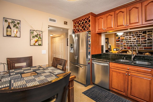 kitchen with stainless steel appliances, dark stone countertops, sink, light tile patterned floors, and a textured ceiling