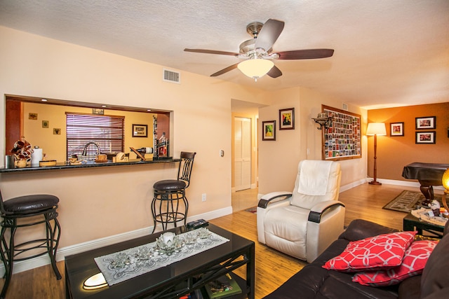 living room featuring light hardwood / wood-style floors, a textured ceiling, indoor bar, and ceiling fan