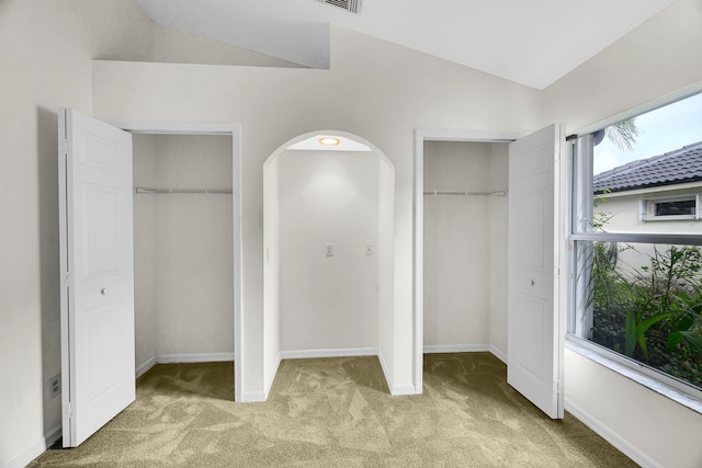 unfurnished bedroom featuring lofted ceiling, light carpet, and multiple closets