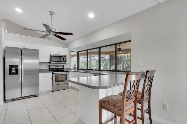 kitchen with kitchen peninsula, a breakfast bar area, appliances with stainless steel finishes, white cabinetry, and vaulted ceiling