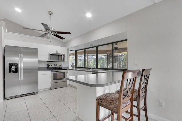 kitchen featuring a peninsula, lofted ceiling, dark countertops, a sink, and stainless steel appliances