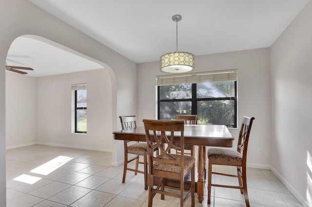 dining space with baseboards, arched walkways, a ceiling fan, and light tile patterned floors