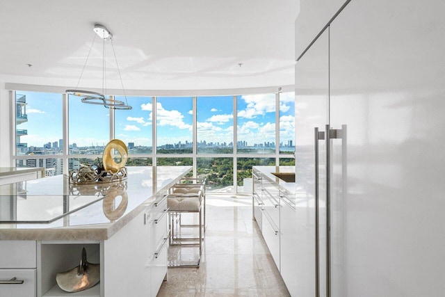 kitchen featuring high end refrigerator, stovetop, pendant lighting, white cabinets, and expansive windows