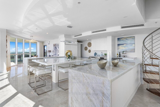 kitchen featuring white cabinetry, a kitchen bar, a spacious island, light stone countertops, and expansive windows