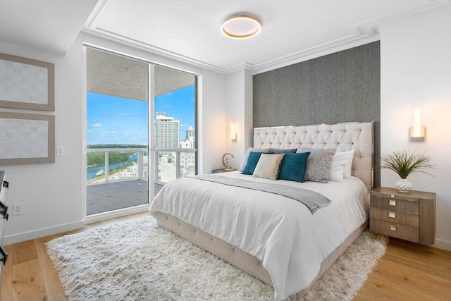 bedroom featuring access to exterior, a wall of windows, light hardwood / wood-style floors, and ornamental molding