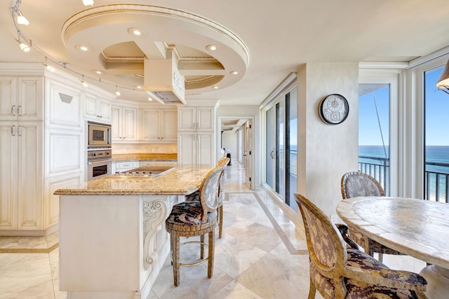 kitchen featuring appliances with stainless steel finishes, a center island, a water view, light stone countertops, and recessed lighting