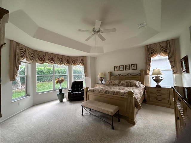 bedroom with a raised ceiling, multiple windows, ceiling fan, and light carpet