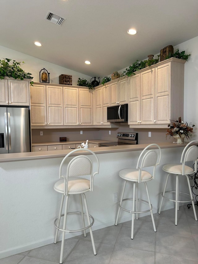 kitchen with a kitchen bar, kitchen peninsula, stainless steel appliances, and light tile patterned floors