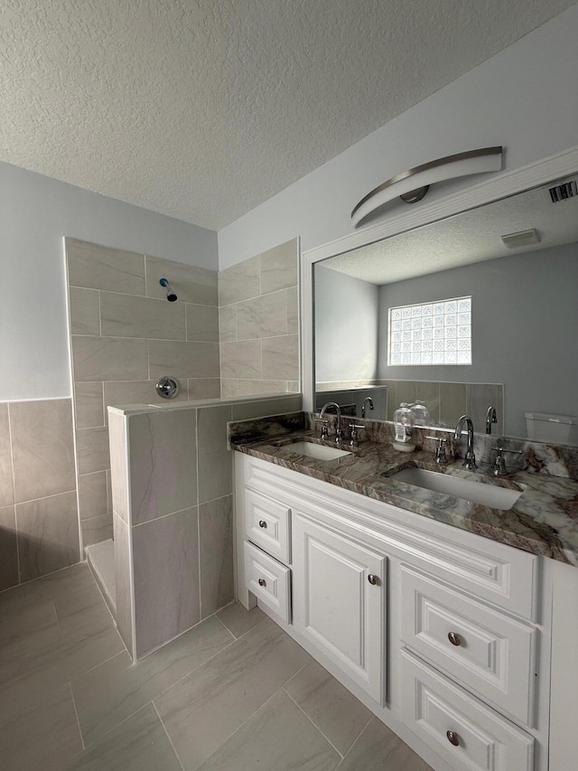 bathroom featuring a tile shower, a textured ceiling, vanity, and tile walls