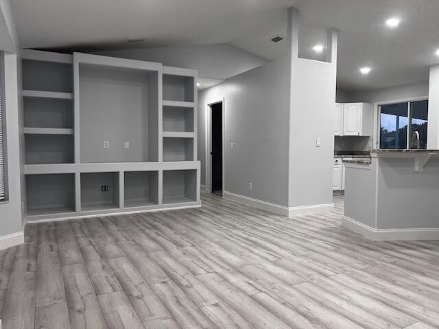 unfurnished living room with vaulted ceiling, light hardwood / wood-style flooring, and built in features