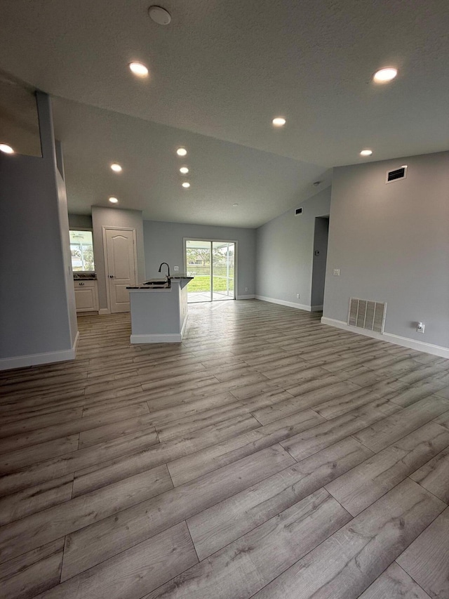 unfurnished living room with vaulted ceiling, sink, and light hardwood / wood-style flooring