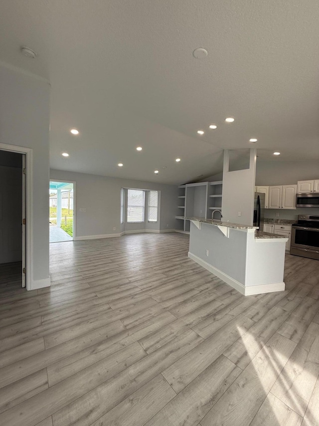 unfurnished living room featuring built in features, lofted ceiling, sink, and light hardwood / wood-style flooring