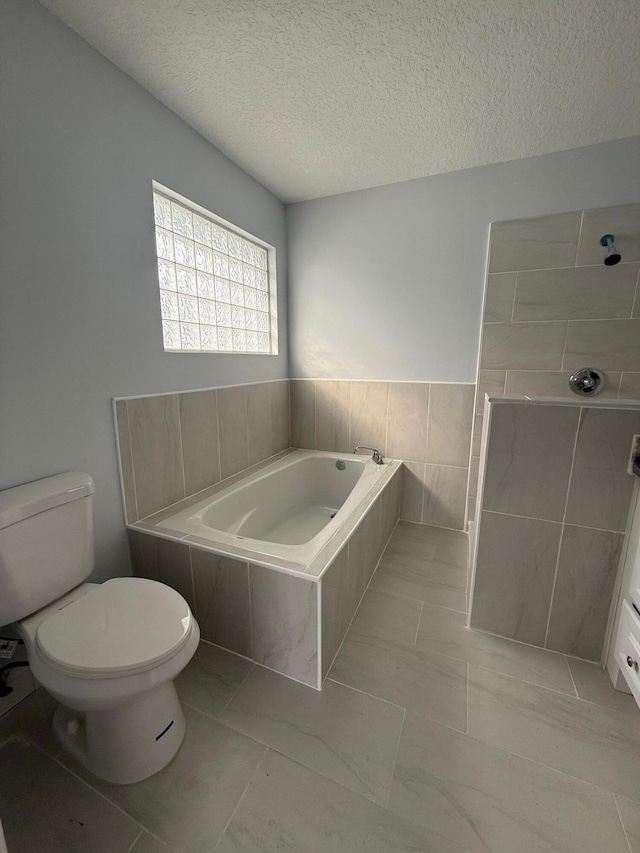 bathroom featuring a textured ceiling, tiled bath, and toilet