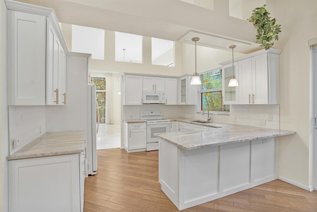 kitchen with sink, white appliances, light stone counters, white cabinets, and kitchen peninsula