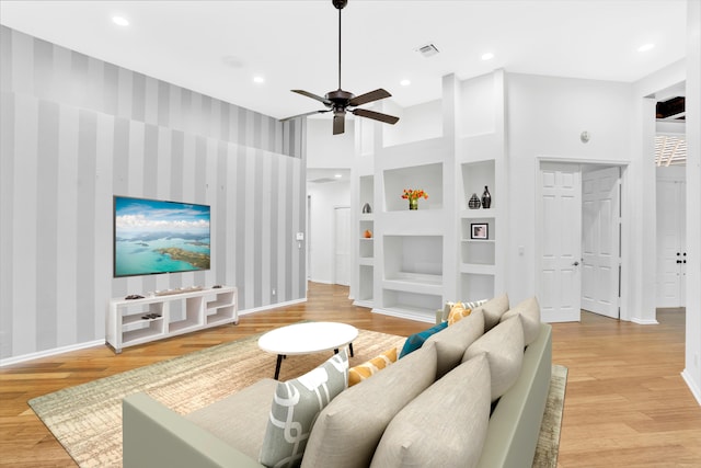 living room featuring built in features, ceiling fan, and light wood-type flooring