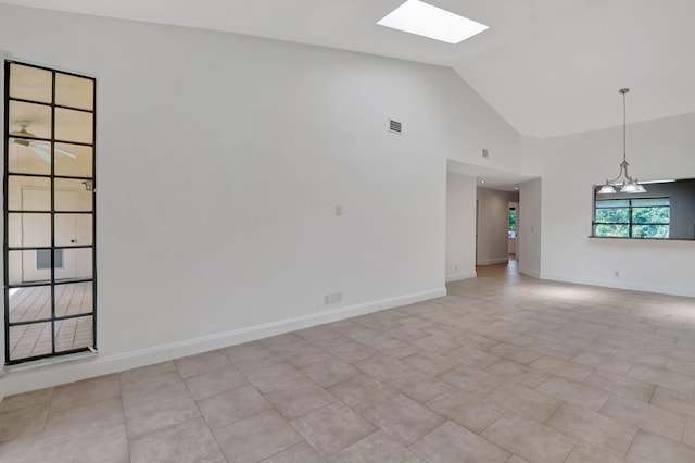 tiled spare room with an inviting chandelier, high vaulted ceiling, and a skylight