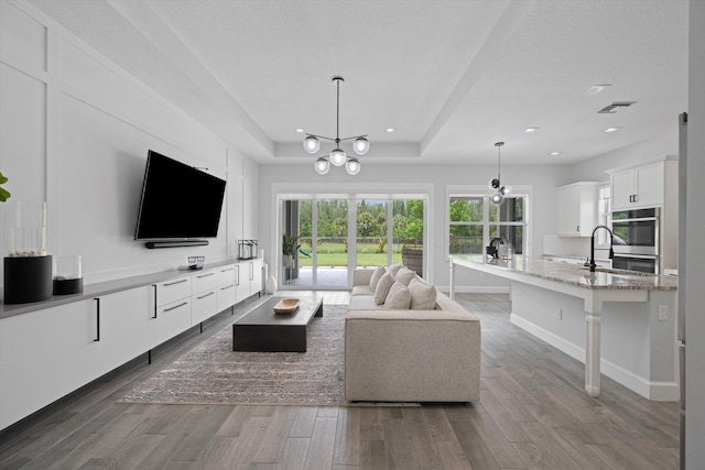 living room with sink, a tray ceiling, and an inviting chandelier