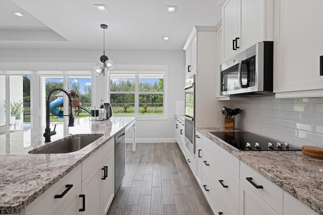 kitchen featuring sink, white cabinetry, hanging light fixtures, stainless steel appliances, and light stone counters