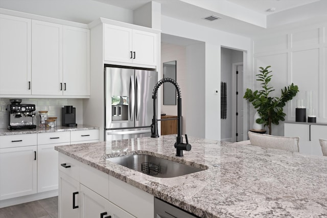 kitchen featuring tasteful backsplash, stainless steel refrigerator with ice dispenser, sink, white cabinetry, and light stone counters