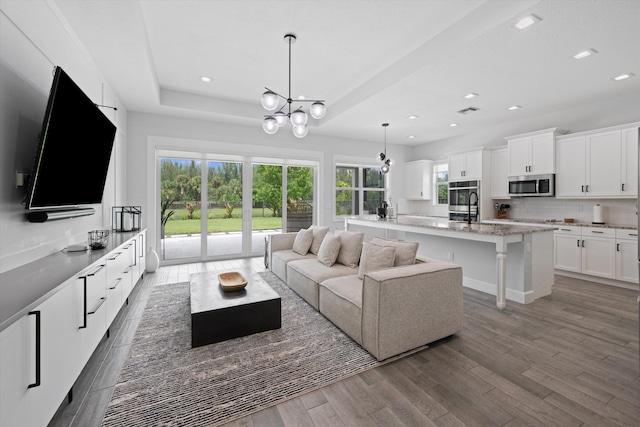 living room featuring hardwood / wood-style floors, a raised ceiling, and an inviting chandelier