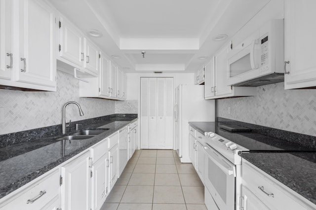 kitchen featuring white appliances, a tray ceiling, a sink, white cabinetry, and light tile patterned flooring
