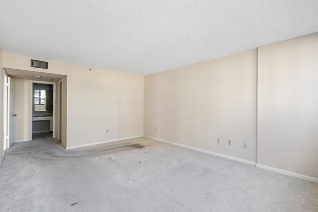 spare room featuring a textured ceiling, light carpet, and baseboards