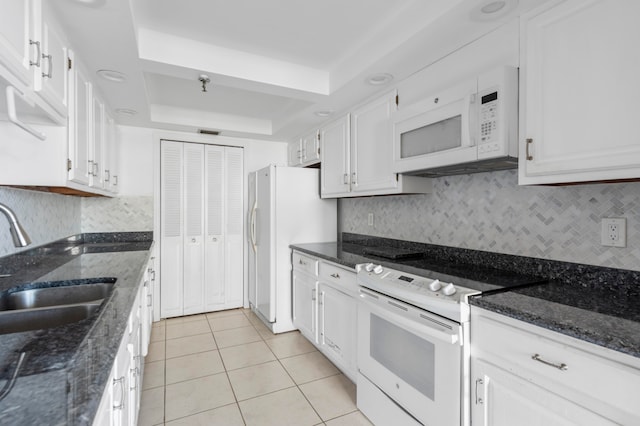 kitchen featuring white cabinetry, a tray ceiling, dark stone countertops, sink, and white appliances