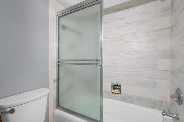 bathroom with toilet and shower / bath combination with glass door