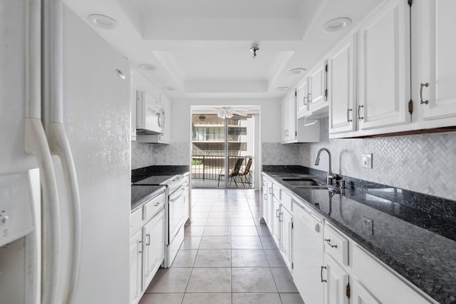 kitchen featuring white cabinets, dark stone counters, white appliances, and a raised ceiling